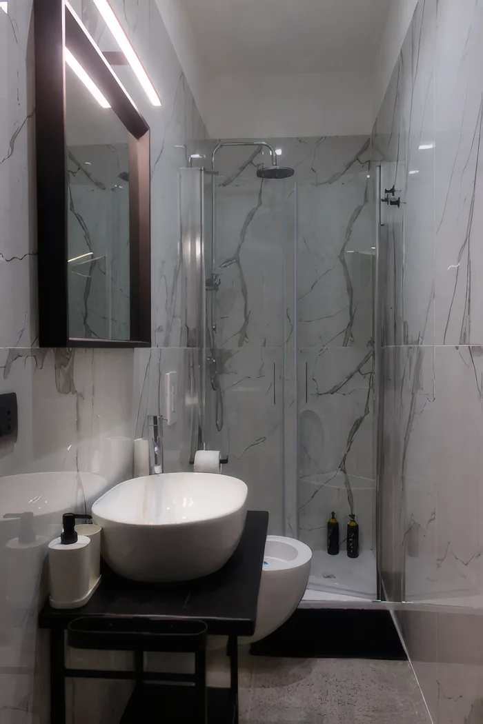Il bagno in marmo bianco, con la doccia, il lavabo e lo specchio illuminato