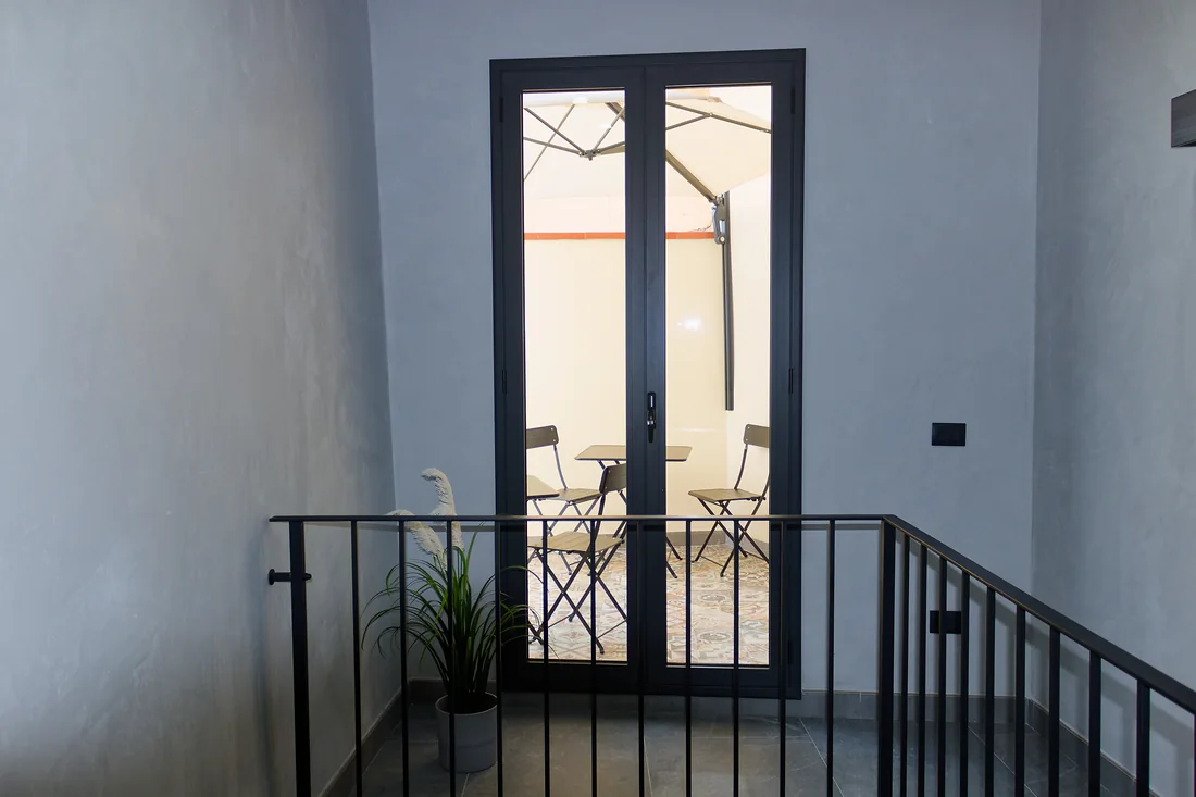 Dal pianerottolo dell'angolo caff&egrave;, la portafinestra che d&agrave; sul terrazzino, oltre la ringhiera della scala