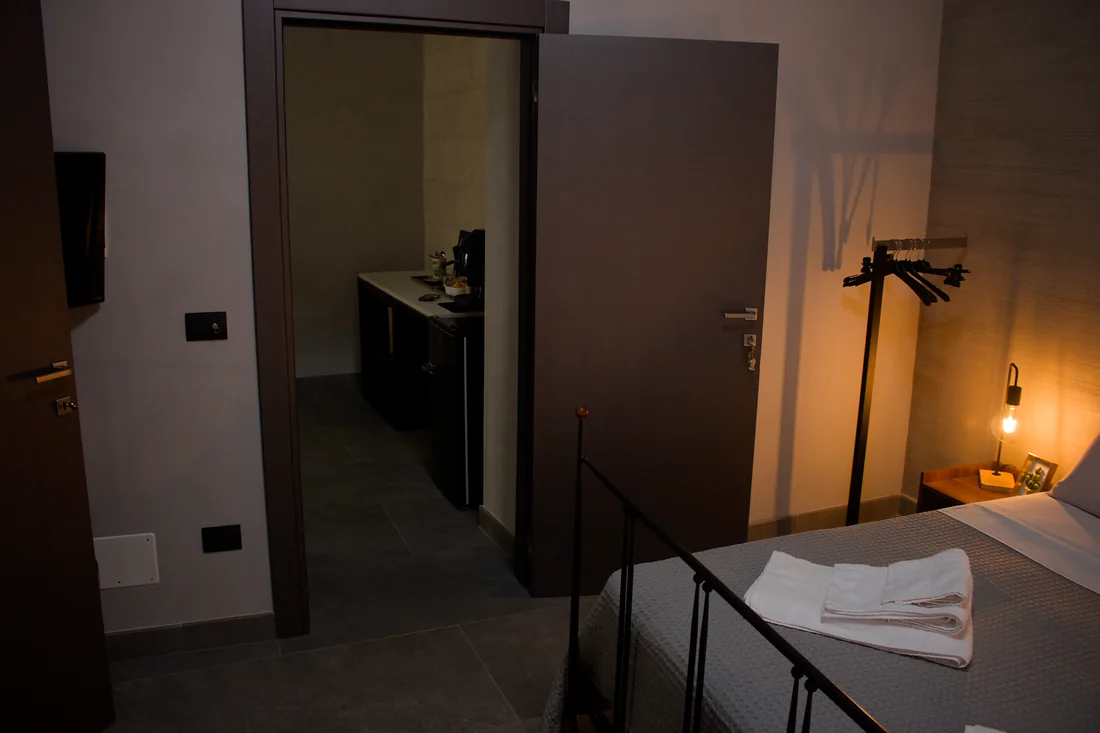 Dalla camera, la porta scorrevole aperta sulla cucina: il piano nero, il frigorifero e, a destra, l'appendiabiti accanto al letto