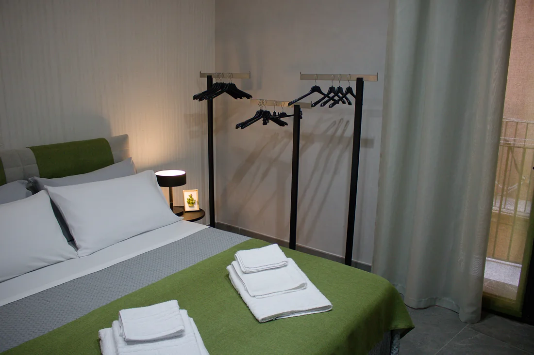 Il letto e, dietro, l'appendiabiti con le grucce; sulla destra la tenda della portafinestra