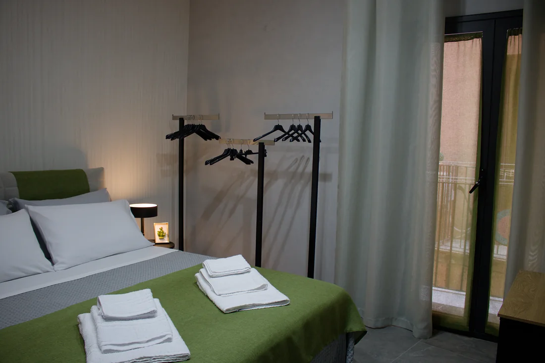 La camera verso il balconcino: il letto, l'appendiabiti e la portafinestra con le tende