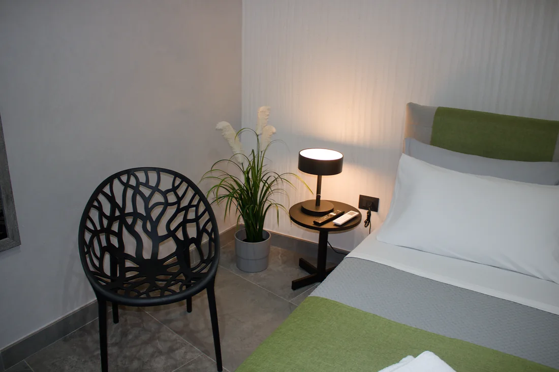 La poltroncina traforata accanto al comodino, con la lampada accesa e la pianta