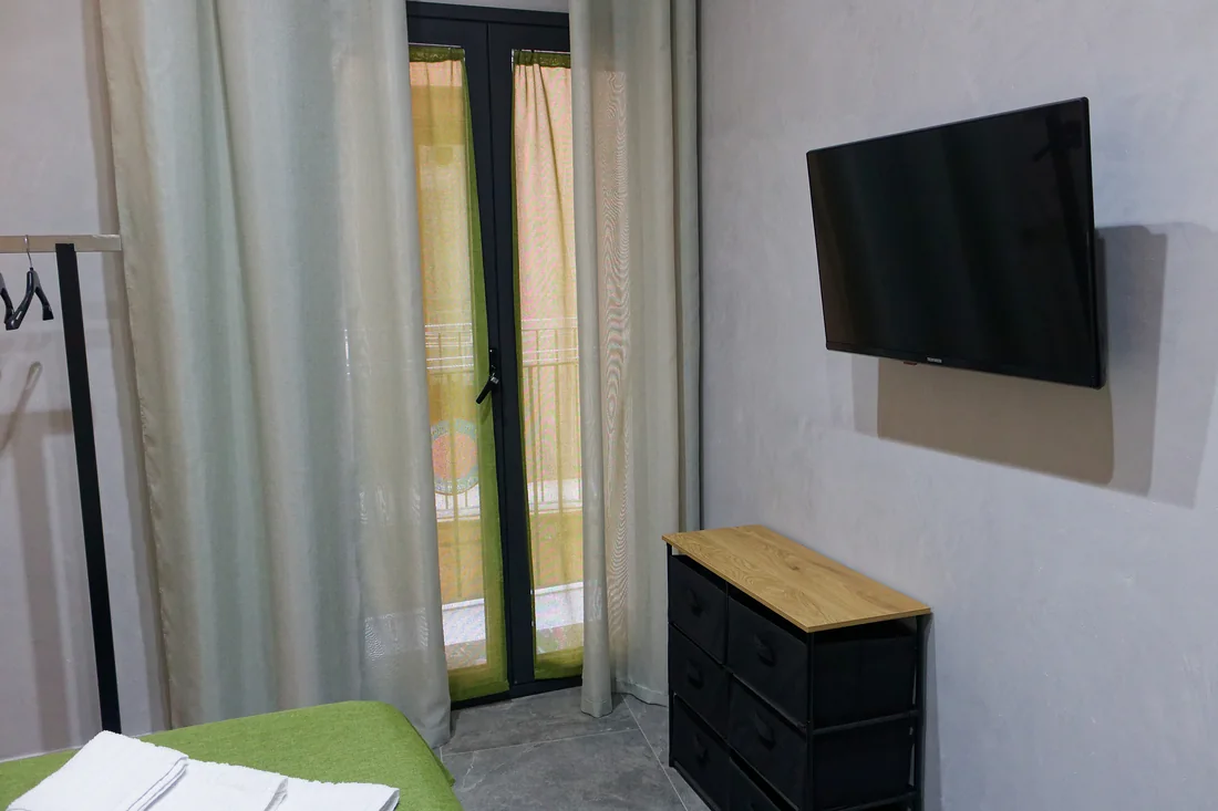 La portafinestra della camera con le tende, il televisore e il cassettone