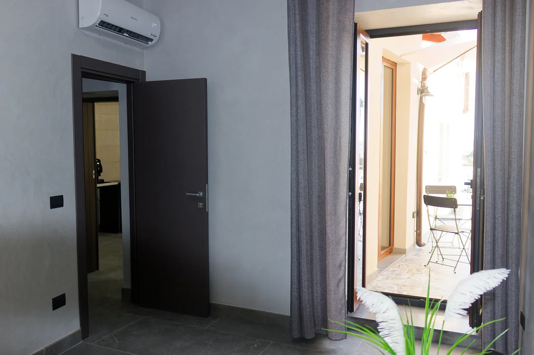 La porta della cucina socchiusa e, accanto, la portafinestra aperta sul terrazzino con il tavolino e l'ombrellone
