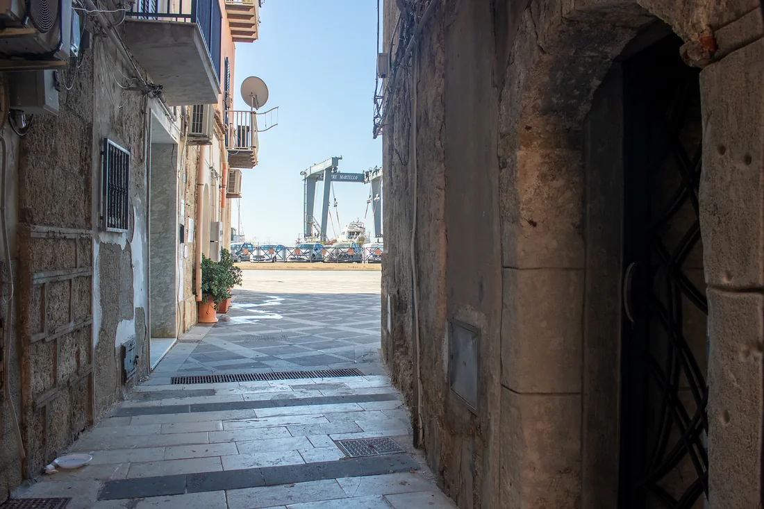 Dal portone, il vicolo che sbocca sulla piazza: in fondo il porto e la gru del cantiere