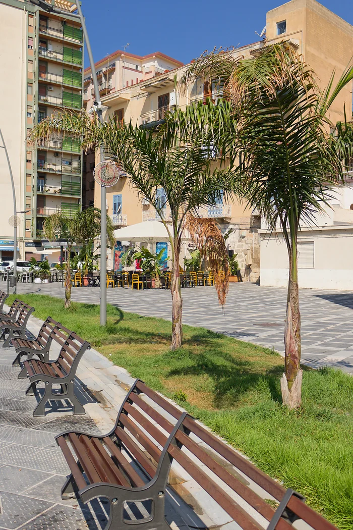 Il lungomare: le panchine di legno e ghisa in fila, le palme piantate sull'erba e, in fondo, i tavolini con le sedie gialle di un locale all'aperto