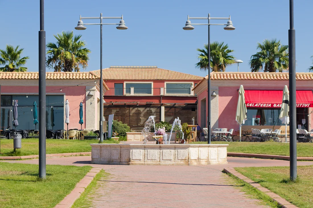 La piazzetta del porto: la fontana in pietra, le palme e i locali con i tavoli fuori