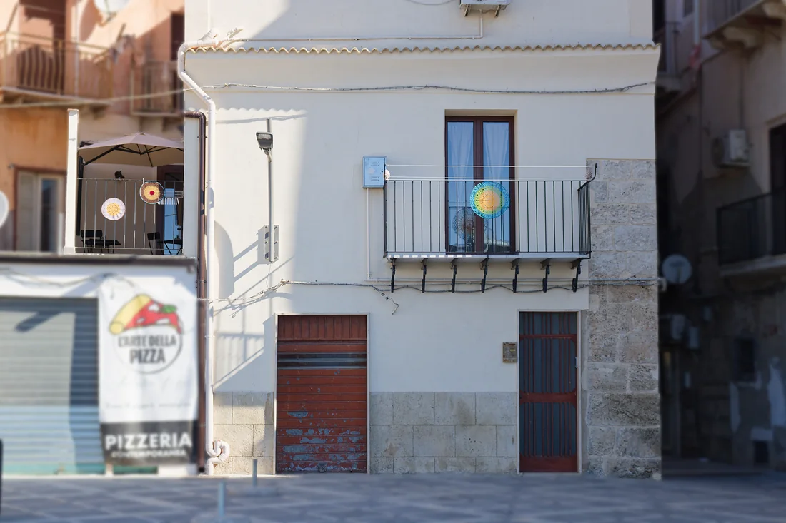 L'ingresso da vicino: il portone di legno, lo zoccolo di pietra e il balconcino con la ringhiera nera