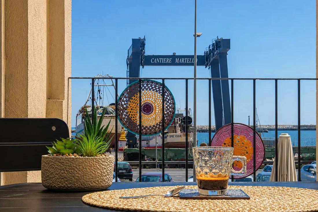 Il caff&egrave; sul tavolo del terrazzino, e dietro la ringhiera il porto con i pescherecci e la gru del cantiere